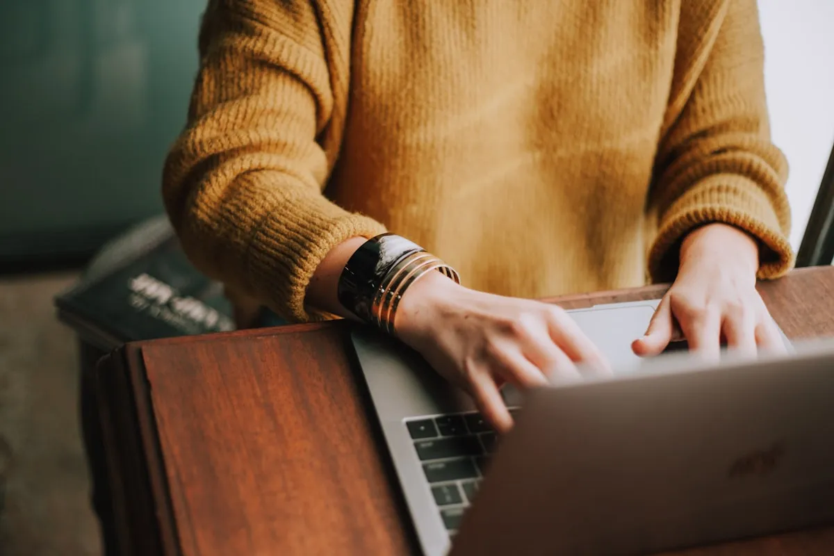 Close-up of hands typing on a laptop at a wooden desk
